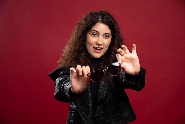 Woman in all black outfit holding glasses and posing.