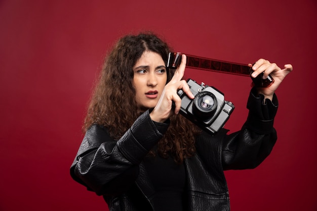 Foto gratuita donna in abito tutto nero che tiene un nastro fotografico con una fotocamera