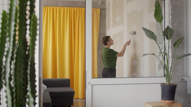 Женщина одна красит стену в своей комнате в сером цвете ремонт дома своими руками в карантине самоизоляции