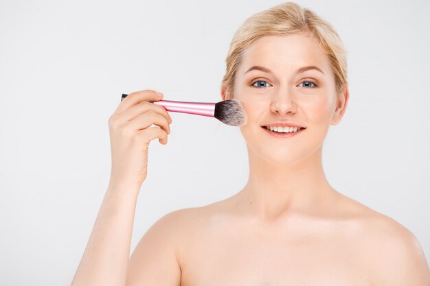 woman apply makeup on face with brush