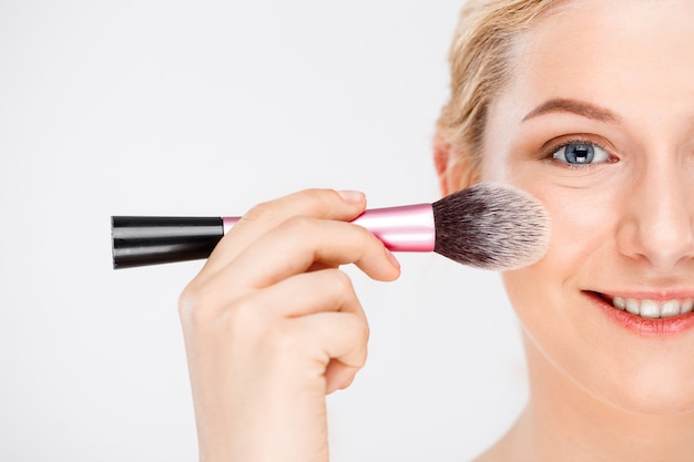 woman apply makeup on face with brush