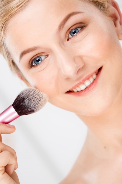 Free photo woman apply makeup on face with brush