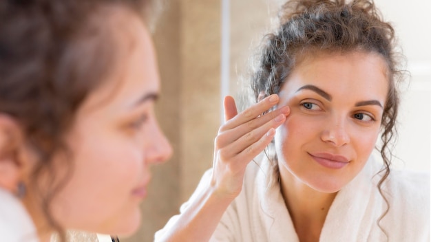 Donna che applica la crema sul viso mentre si guarda allo specchio