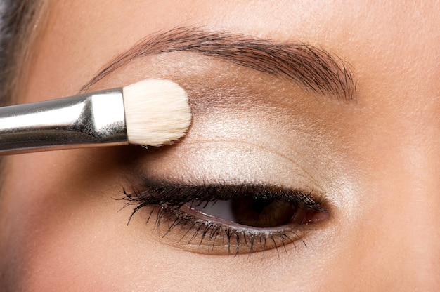 Woman applying eyeshadow on eyelid using makeup brush