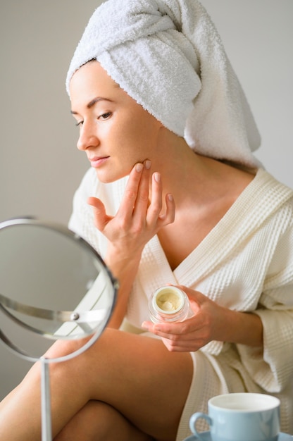 Woman applying face cream at home while looking in the mirror
