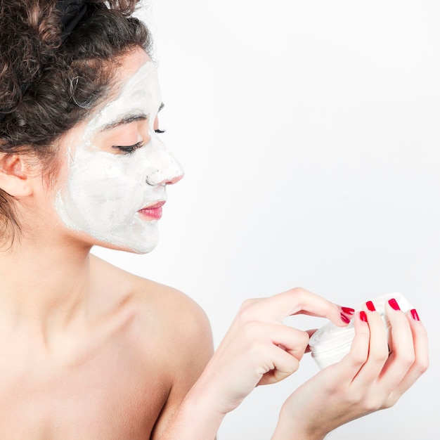 Woman applying facial mask on her face against white background