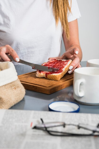 朝食のテーブルでパンのスライスにジャムを適用する女性