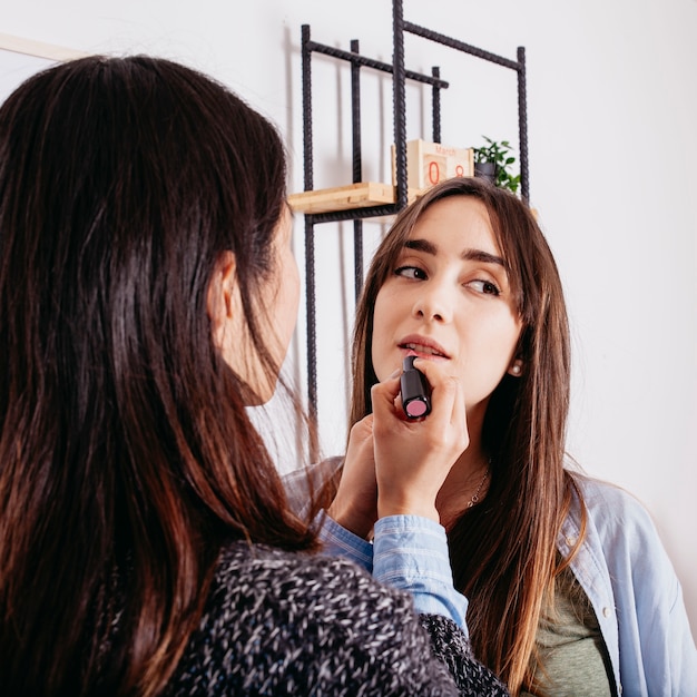 Woman applying lipstick to girlfriend