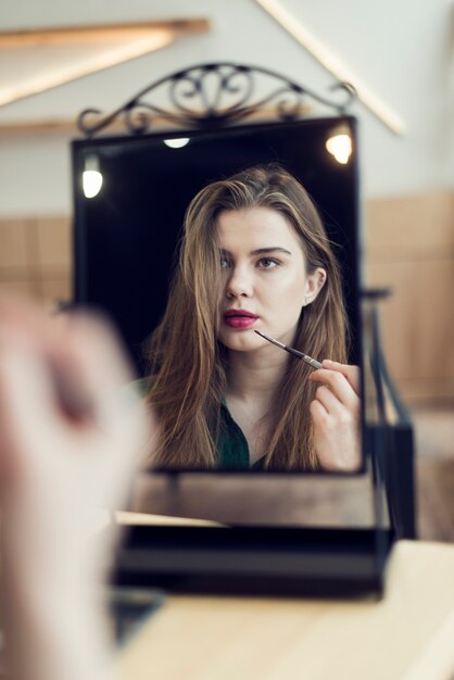 Женщина нанесения макияжа и глядя на зеркало