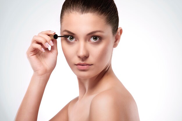 Woman applying mascara on eyelashes