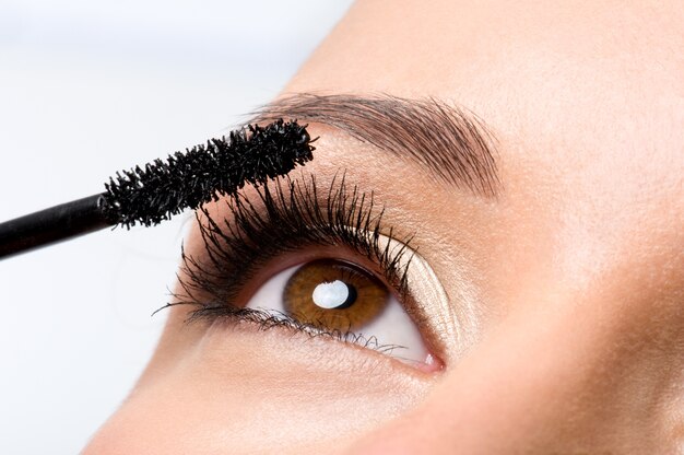 Woman applying mascara on her eyelashes - macro shot