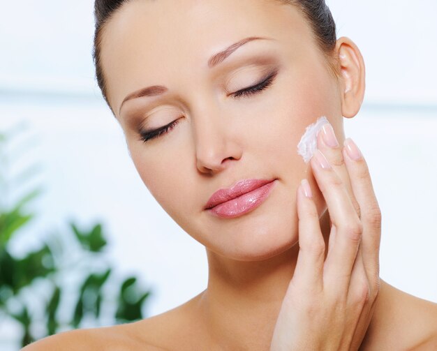 Woman applying  moisturizer cream on her cheek