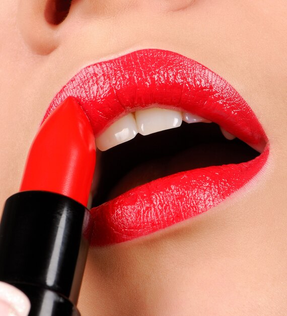 Woman applying red gloss lipstick.