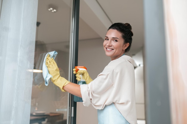A woman in apron cleaning the windows and looking involved
