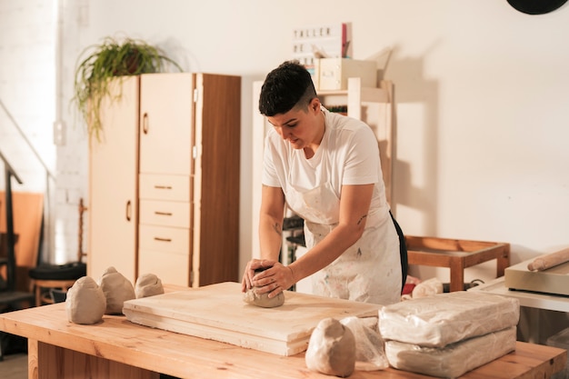 Женщина в фартуке замешивает глину в мастерской