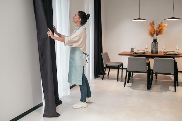 A woman in apron standing near the widnow and looking up