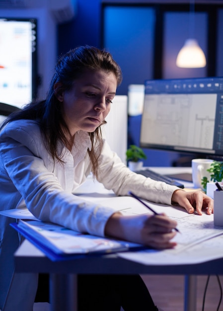 Woman architect analysing and matching blueprints for new building project sitting at desk