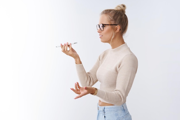 Free photo woman arguing on phone talking via speaker holding smartphone near mouth spread hands in dismay bothered and intense having serious argument sending voice message on white