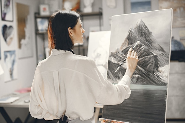 免费照片的女人在一个艺术学校系着围裙在一个画架画。