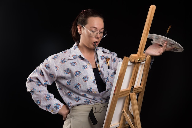 Woman artist holding brush and looking at canvas on black