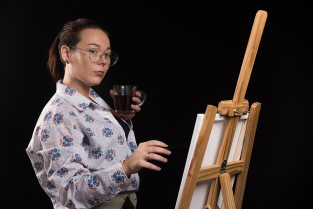 Woman artist holding brush and looking at canvas on black