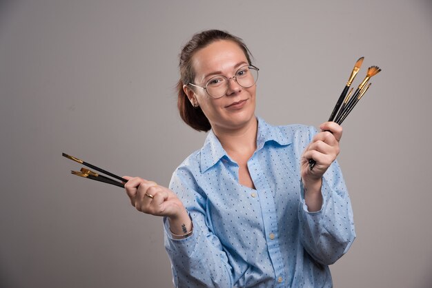 Woman artist holds painting brushes on gray background. High quality photo
