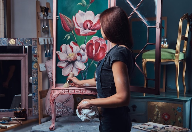 A woman artist painting vintage renovated bookshelf in the workshop.