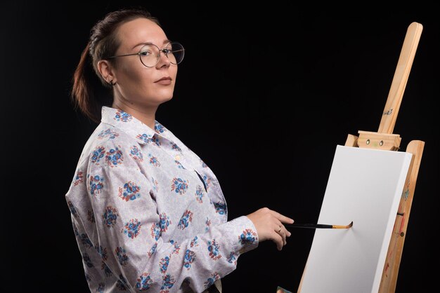 Woman artist paints a picture on canvas with pencil on black