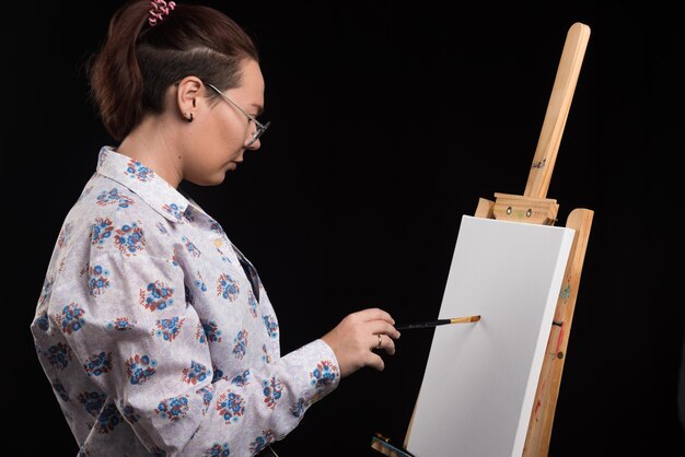 Woman artist paints a picture on canvas with pencil on black