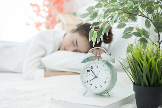 woman asleep in bed while her alarm shows the early time at home in bedroom