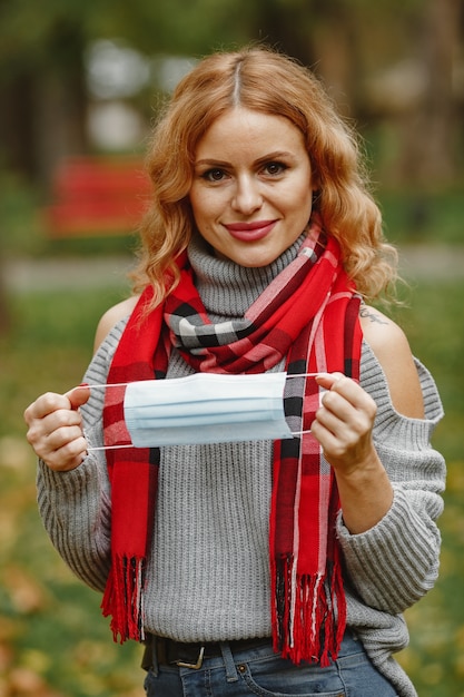 Woman in autumn forest. Person in a mask. Coronavirus theme. Lady in a red scarf.