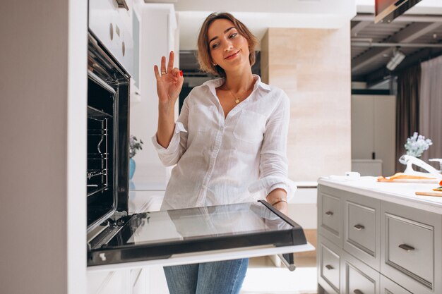 Woman baking at kitchen and looking into the oven