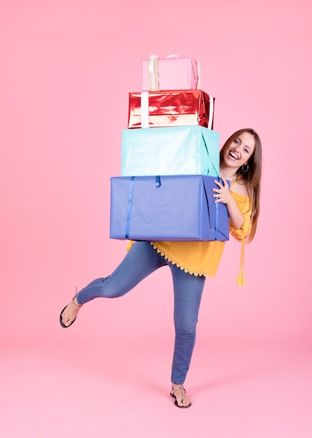 Woman balancing stack of gift boxes on pink background