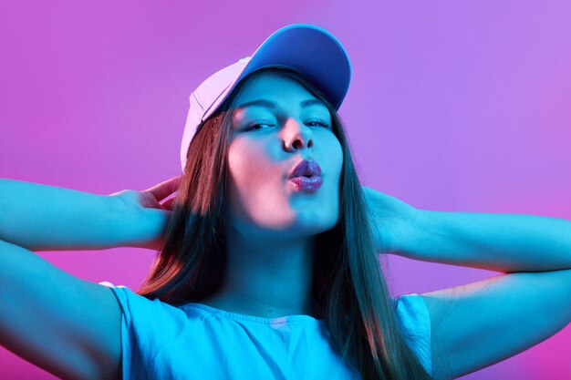 Woman in baseball cap keeping hands behind head and lips rounded