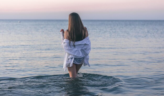 Женщина в купальнике и белой рубашке в море