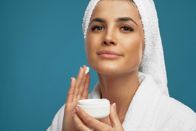 Woman in bathrobe applying cream on face