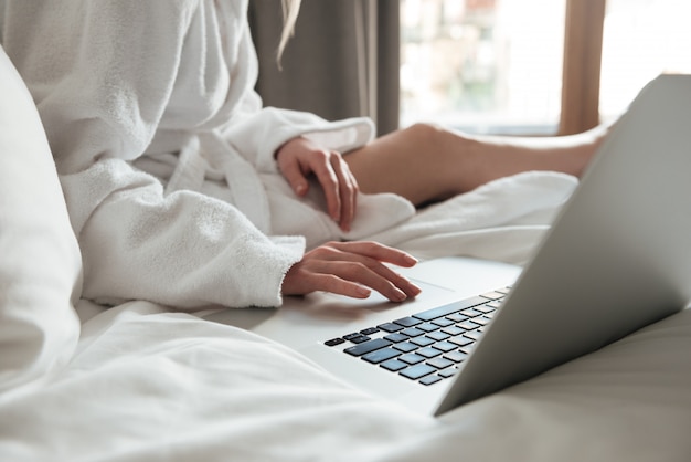 Woman in bathrobe on bed and using laptop