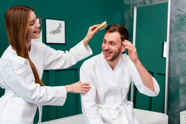 Woman in bathrobe brushing man's hair