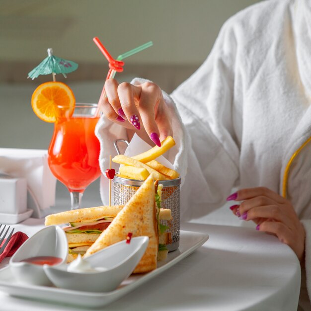 Woman in bathrobe having a meal, eating french fries .