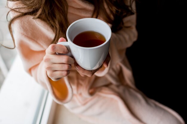 熱いお茶のカップを保持しているバスローブの女性。外気分。