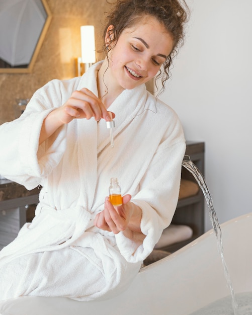 Free photo woman in bathrobe pouring serum in bathtub