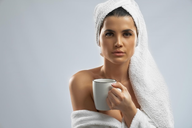 Женщина в халате и полотенце держит чашку