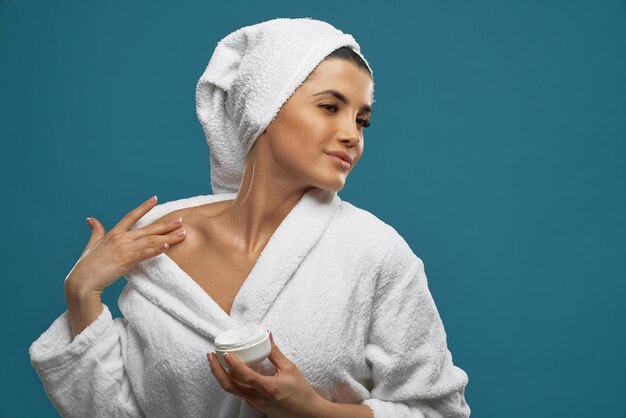 Woman in bathrobe using body cream