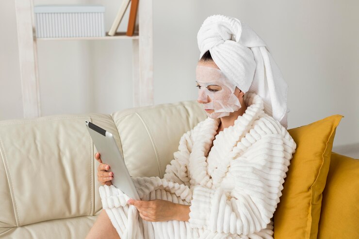 Free Photo woman in bathrobe with facial mask using her tablet