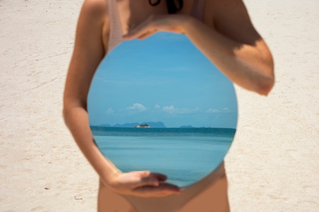 Женщина на пляже летом позирует с круглым зеркалом