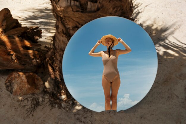 Женщина на пляже летом позирует с круглым зеркалом