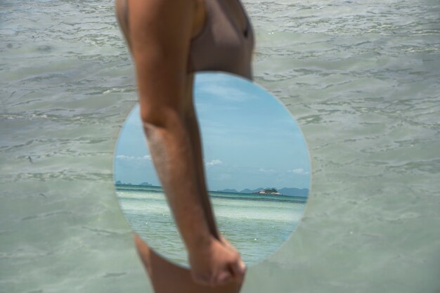 丸い鏡でポーズをとって夏のビーチで女性
