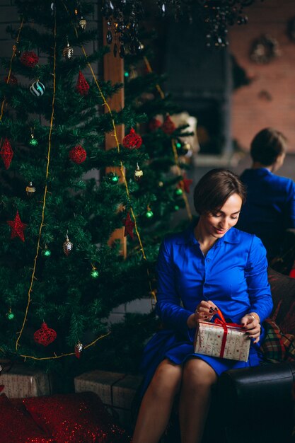 Woman in beautiful dress sitting by Christmas tree