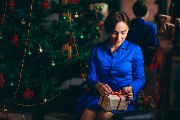 Woman in beautiful dress sitting by Christmas tree
