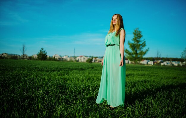 Женщина в красивом длинном бирюзовом платье позирует на лугу на траве